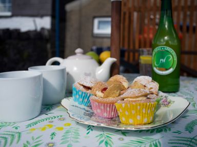 A table with cupcakes in colorful wrappers a teapot two white mugs and a green bottle at 17 Victoria Terrace - Perthi in Nantlle