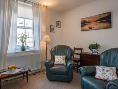 A sitting room with two green armchairs a window with curtains a floor lamp and a wooden table with fruit bowl at 17 Victoria Terrace - Perthi in Nantlle
