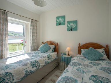 A bedroom with two single beds a bedside table with lamp and books and a window with curtains at 17 Victoria Terrace - Perthi in Nantlle