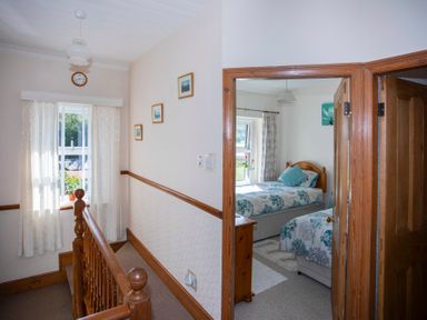 A hallway with wooden banister and clock on wall leading to a bedroom with two single beds at 17 Victoria Terrace - Perthi in Nantlle