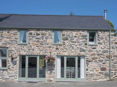 Stone exterior of a cottage with four windows two glass doors and a hanging basket of flowers at Mulberry Cottage in Pentraeth