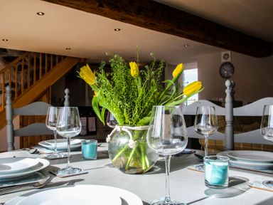 A dining table set with plates glasses and a vase of yellow flowers in a room with wooden stairs at Mulberry Cottage in Pentraeth