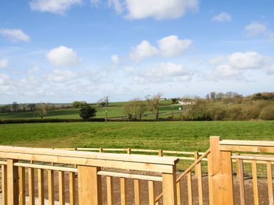 A view of green fields with scattered trees and a wooden fence in the foreground at Mulberry Cottage in Pentraeth