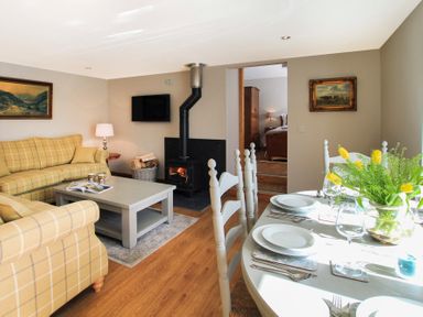 A living room with a wood stove and a dining table set with plates and glasses at Mulberry Cottage in Pentraeth