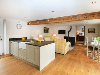 An open kitchen and living area with a wooden floor a kitchen island and yellow plaid sofas at Mulberry Cottage in Pentraeth