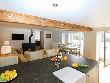 An open plan kitchen and dining area with a black countertop island a sink a dining table with chairs a wood burning stove and a sofa at Mulberry Cottage in Pentraeth