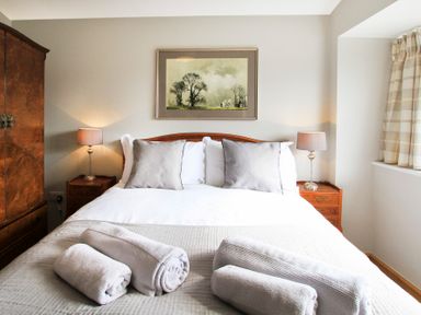 A bedroom with a bed with pillows and rolled towels two bedside tables with lamps a wardrobe and a window with curtains at Mulberry Cottage in Pentraeth