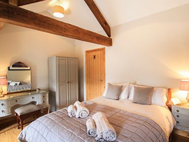 A bedroom with a double bed three rolled towels wooden beams a wardrobe a dressing table and a lamp at Mulberry Cottage in Pentraeth