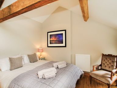 A bedroom with a bed a side table with lamp a framed picture on the wall and an armchair at Mulberry Cottage in Pentraeth
