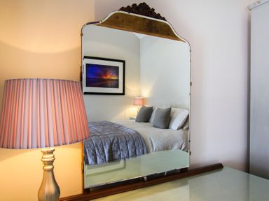 A mirror reflecting a bedroom with a bed gray pillows a lamp and a framed picture at Mulberry Cottage in Pentraeth
