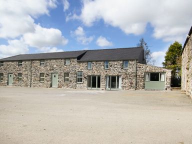 A stone building with multiple windows and doors under a blue sky at Mulberry Cottage in Pentraeth