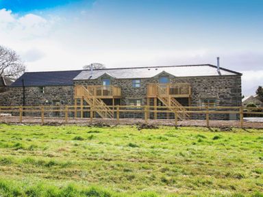 A stone house with two wooden staircases and balconies in a grassy field at Mulberry Cottage in Pentraeth