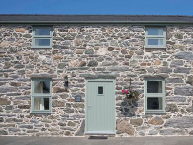 Exterior view of a stone cottage with four windows and a centered front door with flower pot at Partridge Cottage in Menai Bridge