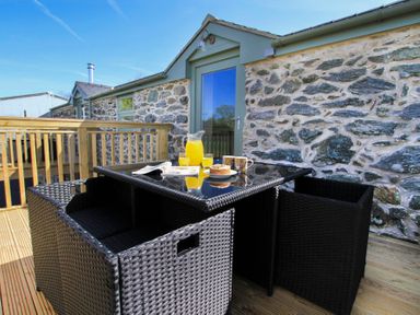 A patio with a black wicker table and chairs a jug of orange juice two glasses a cake and two mugs at Partridge Cottage in Menai Bridge