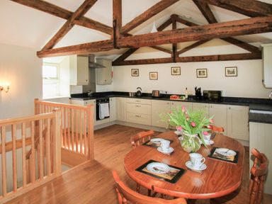 A kitchen with wooden beams a round wooden dining table set with cups and plates and cream cabinets at Partridge Cottage in Menai Bridge