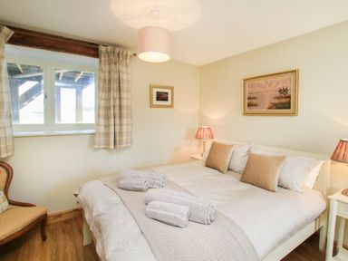 A bedroom with a double bed bedside tables lamps a chair and two framed pictures on the walls at Partridge Cottage in Menai Bridge