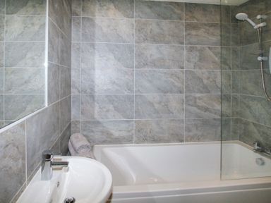 A bathroom with a bathtub shower and sink with towels on the edge at Partridge Cottage in Menai Bridge