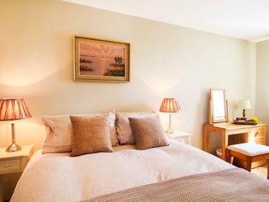 A bedroom with a bed pillows bedside tables lamps a dressing table with a mirror and a stool at Partridge Cottage in Menai Bridge
