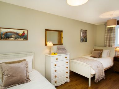 A bedroom with two single beds a white chest of drawers and framed pictures at Partridge Cottage in Menai Bridge