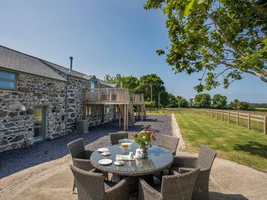 A stone building with an outdoor dining table and chairs on a patio near a grassy area at Partridge Cottage in Menai Bridge