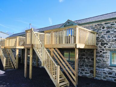 A stone building with two wooden decks and stairs outside at Partridge Cottage in Menai Bridge