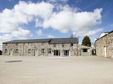 A long stone building with multiple windows and green doors under a partly cloudy sky at Partridge Cottage in Menai Bridge