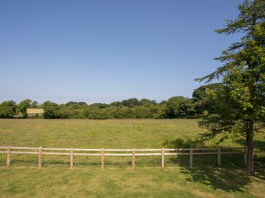 A field with a wooden fence and trees under a clear blue sky at Partridge Cottage in Menai Bridge