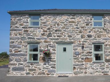 Stone cottage with green door and windows and a hanging flower basket at Teal Cottage in Menai Bridge