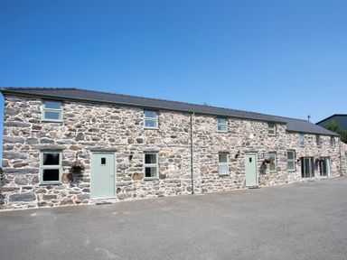 A long stone building with multiple windows and doors under a clear sky at Teal Cottage in Menai Bridge