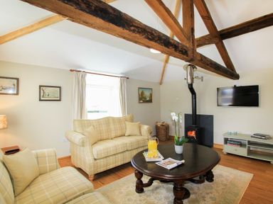 A living room with exposed wooden beams sofas a coffee table a wood stove and a wall mounted TV at Teal Cottage in Menai Bridge