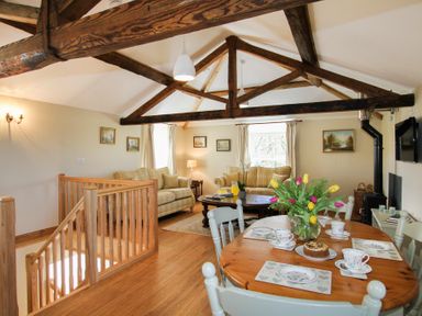 An open living and dining room with wooden beams wooden floors a dining table with cups a cake and flowers and sofas at Teal Cottage in Menai Bridge