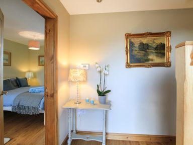 A small table with a lamp, two candles, and a potted plant next to a doorway showing a bedroom with a bed and lamps at Teal Cottage in Menai Bridge