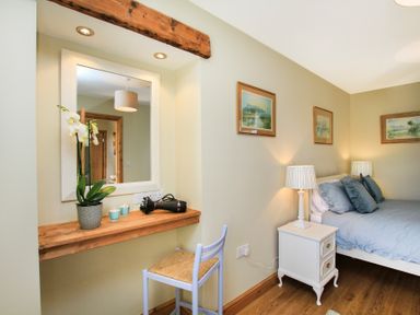 A bedroom with a bed bedside table lamps framed pictures a wooden shelf with a mirror a hairdryer and a plant Teal Cottage Menai Bridge