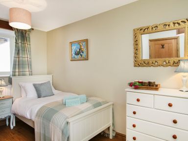 A bedroom with a single bed a nightstand with lamp a chest of drawers with a mirror and a painting at Teal Cottage in Menai Bridge