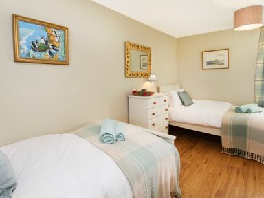 A bedroom with two single beds teddy rugs a chest of drawers and framed pictures on the walls at Teal Cottage in Menai Bridge