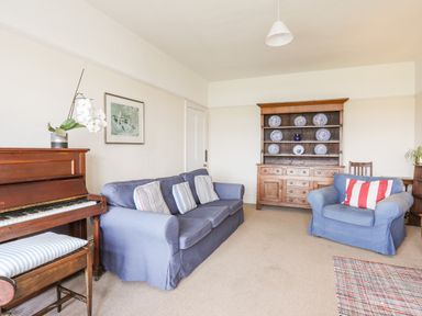 A living room with a blue sofa and armchair a wooden piano and cabinet with decorative plates at Windygates in Rhosneigr