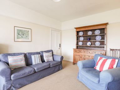 A living room with blue sofa and armchair with cushions a wooden dresser with blue and white plates on shelves and a framed picture on the wall at Windygates in Rhosneigr