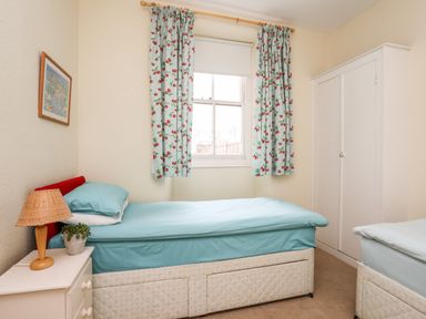 A bedroom with two single beds a window with floral curtains a bedside table with a lamp and plant and a white wardrobe at Windygates in Rhosneigr