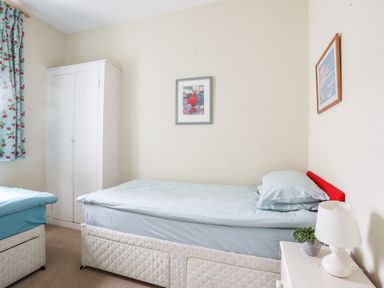 A bedroom with two single beds a white wardrobe a bedside table with a lamp and plant and framed pictures on the wall at Windygates in Rhosneigr