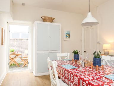 A dining room with a red patterned tablecloth on a table set with plants glasses and placemats at Windygates in Rhosneigr