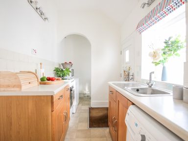 A narrow kitchen with wooden cabinets white countertops a sink and window with flowers at Windygates in Rhosneigr