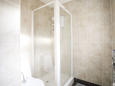 A bathroom with a toilet and a glass shower enclosure with beige tiled walls at Windygates in Rhosneigr