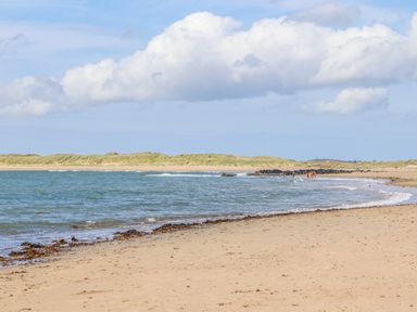 A sandy beach with seaweed along the shore and people near the water at Windygates in Rhosneigr