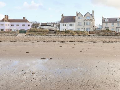 A sandy beach with seaweed patches in front of residential houses at Windygates in Rhosneigr