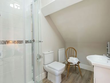A bathroom with a shower, toilet, sink, and a chair at West View in Rhosneigr
