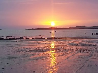 A sunset over the ocean with people standing on the sand at West View in Rhosneigr
