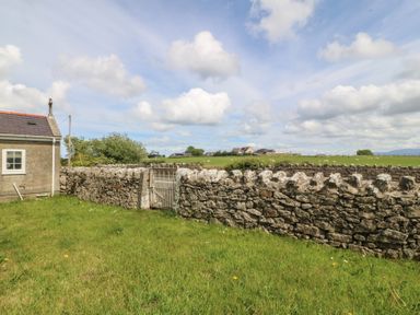 An outdoor view showing a house and a stone wall with a gate in Llanallgo Church Rooms 