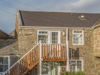 A stone building with external wooden stairs and white framed windows at Potters by the Sea in Sennen