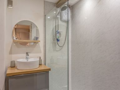 A bathroom with a round mirror above a sink and a shower with a glass door at Potters by the Sea in Sennen