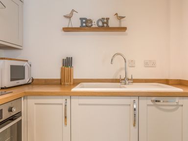 A kitchen countertop with a sink a knife block a microwave and wall decorations at Potters by the Sea in Sennen
